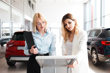 Saleswoman shows  a specification about a car to a young woman. Business lady chooses a new car