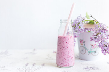 Berry smoothie in a glass jar with a straw for cocktails,lilac branch in a bucket with a pattern ladies bike on light background.Diet, detox.Refusal of plastic.Daylight, selective focus.Space for text