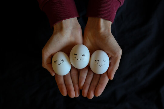 Chicken eggs with painted face on a black background. Hand-painted eggs / Easter eggs / natural white eggs decorated with hats and animated baby look.