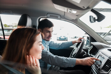 Joyful young couple sitting in a car dealership inside their new car