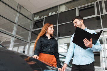 Salesman shows the car to a young client of a car dealership