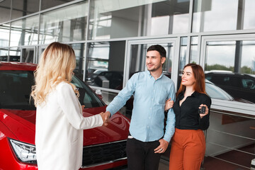 Family couple at car dealership. 
Husband shakes hands with a car dealer after a successful deal