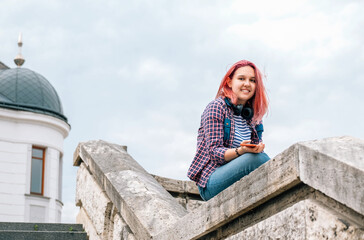 Portrait of cheerfully smiling Beautiful modern young female teenager with extraordinary hairstyle color in checkered with headphones on the neck. Modern teens or cheerful students concept image.