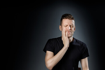 Young man, showing painfull, toothache emotions on black background.
