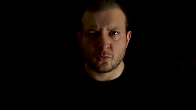 Serious young male portrait on black background. Face of psycho, crazy angry man, Horror and mysterious concept. Dangerous man.