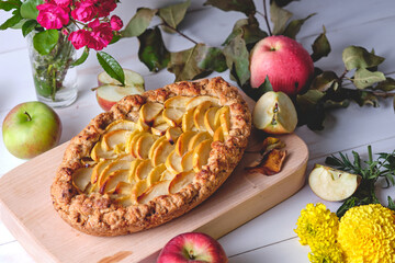 Homemade apple pie on a blackboard. Dessert on a white wooden table, apples and flowers lie around.