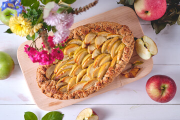 Homemade apple pie on a blackboard. Dessert on a white wooden table, apples and flowers lie around. Top view.