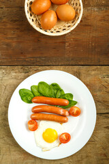 Fried egg with sausages and cherry tomatoes in a white plate on a wooden table.