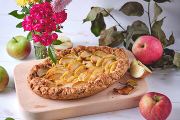 Homemade apple pie on a blackboard. Dessert on a white wooden table, apples and flowers lie around.