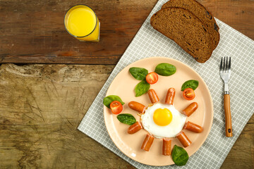 Scrambled eggs with sausages in the shape of a sun children's breakfast m glass of juice.