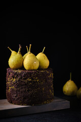 Chocolate cake decorated with ground pistachios and fresh pears on a wooden board.