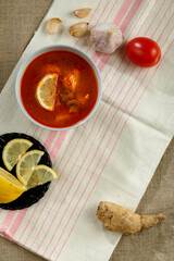 Plate with thai tom yam soup on a linen tablecloth and linen napkin and garlic and lemon nearby.