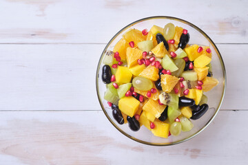 Fruit salad in a transparent glass bowl on a white wooden table.