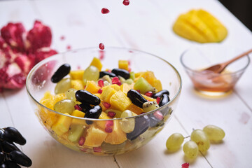 Fruit salad in a transparent glass bowl on a white wooden table.