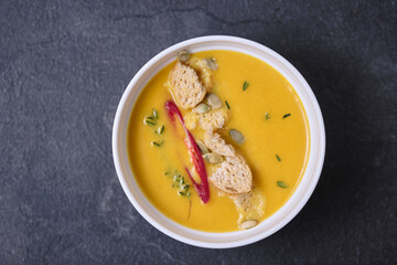 Pumpkin cream soup with breadcrumbs, hot pepper and thyme, garnished with pumpkin seeds. Top view.