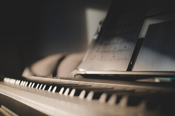 Low shot of 88 keys of a keyboard and sheet music. Close up with light from side