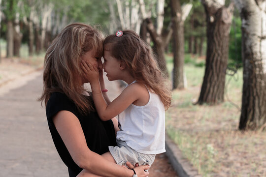Beautiful Caucasian mother stands and holding her cute joyful blonde girl  in her arms and kissing her kid with love while the child closing the eyes. Touch of mother's love concept.