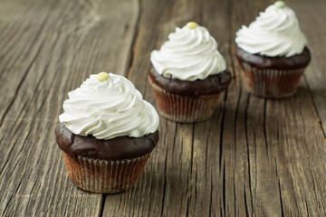 Chocolate cupcakes in paper patty cases, topped with whipped cream and decorated with button-shaped candies, on the rustic wood planks.