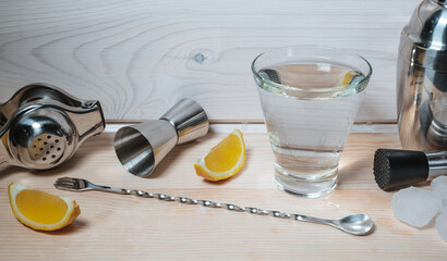 Professional bartender tools for making cocktails on wooden background. Pieces of ice and lemon near the glass of alcohol or non alcohol liquid water are ready to make mixed drinks. Healthy beverage.