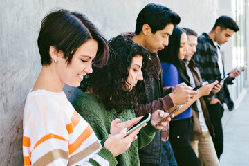 Group of young adults stare at their cell phones while standing against a wall in the city - Millennial - Technology