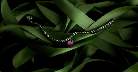 Female silver bracelet with pink heart laying on green fabric strings