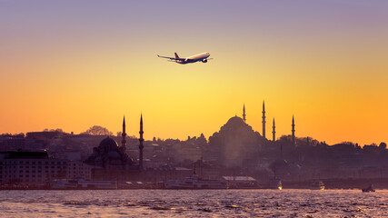 Skyline of Istanbul at sunset with silhouettes of mosques and old buildings in Sultanahmet district. Cityscape of Istanbul with passenger airplane over the ancient downtown in sun lights.
