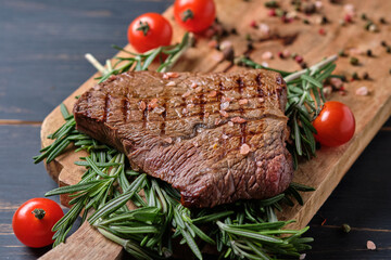 Freshly cooked steak on rosemary branches. Dish served on a large wooden board with cherry tomatoes. Close-up.