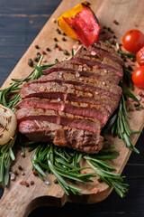 Sliced freshly cooked steak with blood, served with grilled vegetables and fresh rosemary on a wooden board. Close-up.