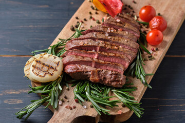 Sliced freshly cooked steak with blood, served with grilled vegetables and fresh rosemary on a wooden board. Close-up.
