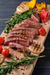 Sliced freshly cooked steak with blood, served with grilled vegetables and fresh rosemary on a wooden board. Close-up.