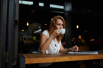 Young charming woman posing while sitting in cafe during coffee break,