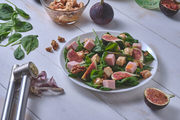 The process of making salad with figs. Ready salad and ingredients on a white wooden table.