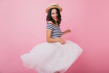 Fototapeta premium Graceful brunette girl dancing with excited smile. Adorable woman in hat and skirt posing on pastel background and looking to camera.