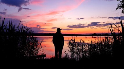 The black silhouette of a man near the lake, which reflects the sunset sky