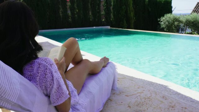 WS Woman reading book on lounge chair by pool 