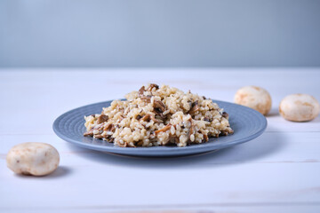 Risotto with mushrooms close-up on a gray plate. Italian dish on a white wooden table.