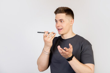 A young man, a guy talking to a friend on the phone, recording a voice message or a note in a smartphone application, holding a mobile phone near his lips close to the speaker, talking to an assistant - Powered by Adobe