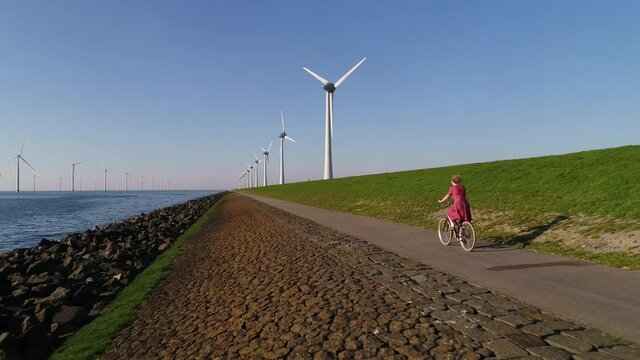 WS AERIAL POV TS SLO MO Girl cycling on road along wind farm / Urk, Flevoland, Netherlands