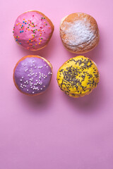 Four donuts with colored glaze on a pink paper background.