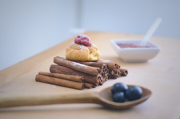 Postre de arequipe con dulce de frutos rojos servido sobre palitos de canela junto a uvas en una cuchara de madera y algunos palitos de canela sobre una mesa de madera. Repolla de arequipe. Repostería