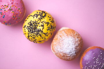 Four donuts with colored glaze on a pink paper background.