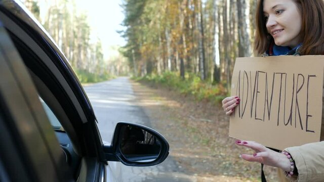 a car stops next to a woman tourist with an adventure sign