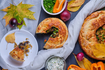 Sliced piece of homemade autumn pie with meat, onions and bell pepper on a plate. Dish on a dark wooden table. Top view.