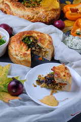 Sliced piece of homemade autumn pie with meat, onions and bell pepper on a plate. Dish on a dark wooden table.