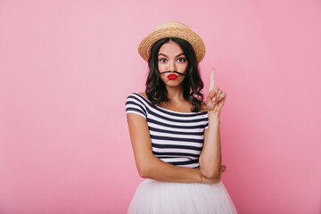Interested brunette girl with red lips fooling around on pink background. Studio portrait of blithesome caucasian woman posing in stylish straw hat.