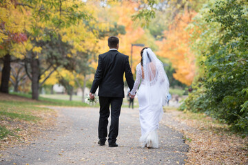 The groom and the bride walk holding hands in the autumn park.