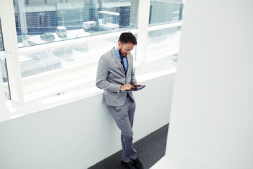 Half length portrait of rich businessman holding portable digital tablet during work break in hallway