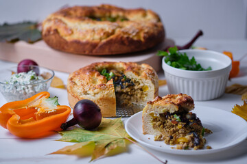 Homemade autumn pie with meat, onions and bell pepper on the board. Dish on a white wooden table. Close-up.