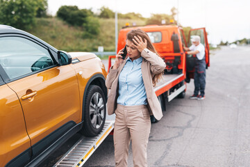 Elegant middle age business woman calling someone while towing service helping her on the road. Roadside assistance concept.