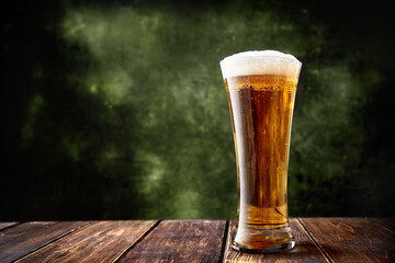 Long glass of beer on dark green background and wooden table with copy space